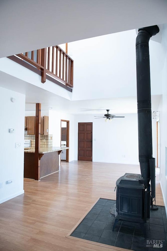 living room with wood finished floors, ceiling fan, baseboards, a wood stove, and a towering ceiling