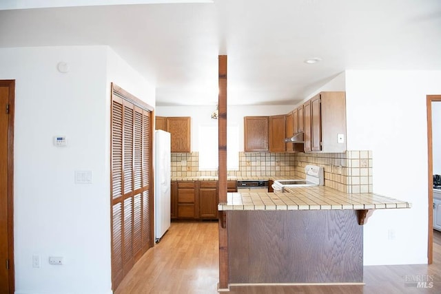 kitchen featuring electric stove, tasteful backsplash, tile counters, under cabinet range hood, and a peninsula