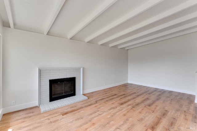 unfurnished living room featuring a brick fireplace, beamed ceiling, baseboards, and wood finished floors