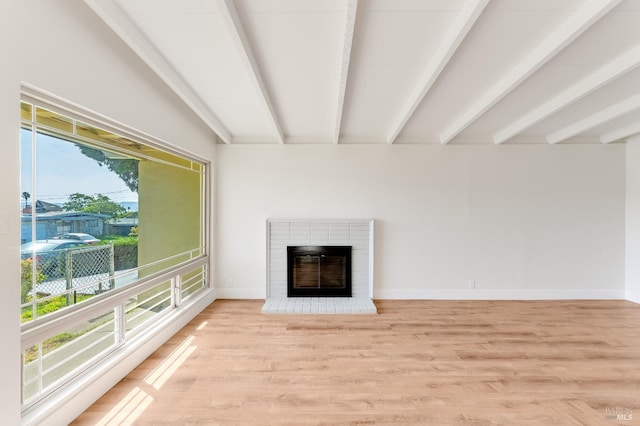 unfurnished living room featuring lofted ceiling with beams, baseboards, a fireplace, and light wood-style flooring