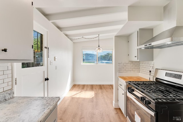 kitchen featuring stainless steel gas range oven, light wood-type flooring, light countertops, wall chimney exhaust hood, and backsplash
