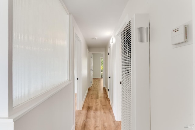 hallway featuring baseboards, a heating unit, and light wood-style flooring