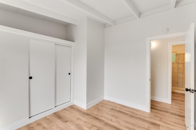 unfurnished bedroom with light wood-style floors, baseboards, a closet, and beamed ceiling