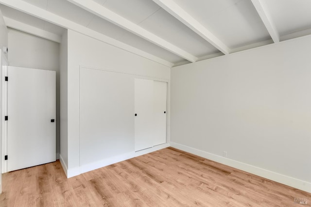 unfurnished bedroom featuring baseboards, lofted ceiling with beams, a closet, and light wood finished floors
