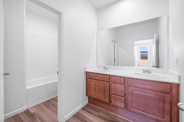 bathroom with a sink, double vanity, wood finished floors, and a tub