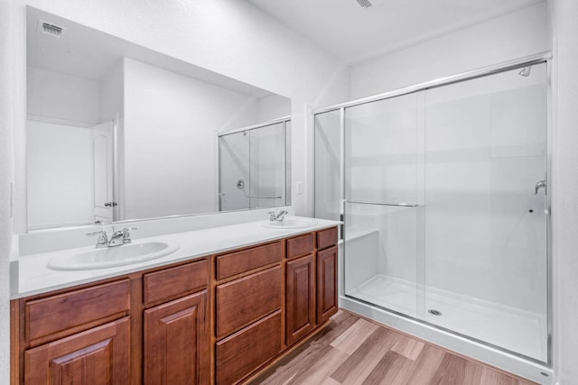 full bathroom with visible vents, a sink, a stall shower, and wood finished floors