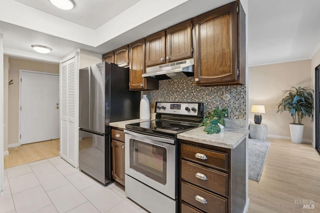 kitchen with tasteful backsplash, under cabinet range hood, baseboards, light wood-style floors, and appliances with stainless steel finishes