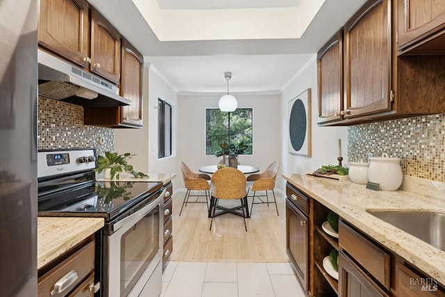 kitchen with ornamental molding, stainless steel appliances, a raised ceiling, under cabinet range hood, and backsplash