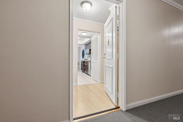 corridor with a textured wall, carpet floors, ornamental molding, and baseboards