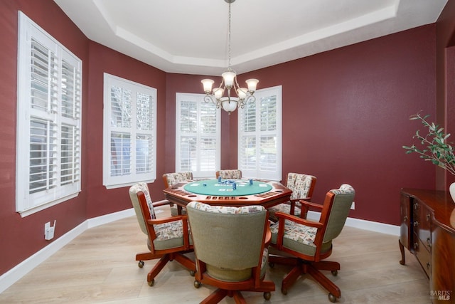 dining area with light wood finished floors, baseboards, a chandelier, and a raised ceiling