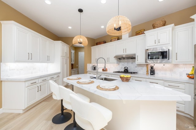 kitchen with white cabinets, a sink, stainless steel appliances, and under cabinet range hood