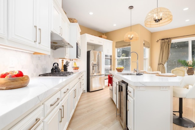kitchen with stainless steel appliances, under cabinet range hood, wine cooler, a sink, and light wood finished floors