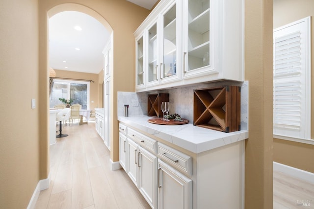 bar featuring recessed lighting, light wood-type flooring, baseboards, backsplash, and arched walkways
