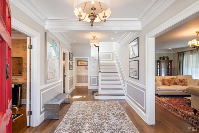 entryway featuring crown molding, stairs, wainscoting, wood finished floors, and a notable chandelier