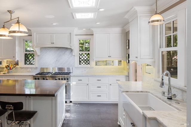 kitchen with stainless steel stove, a sink, white cabinetry, and tasteful backsplash