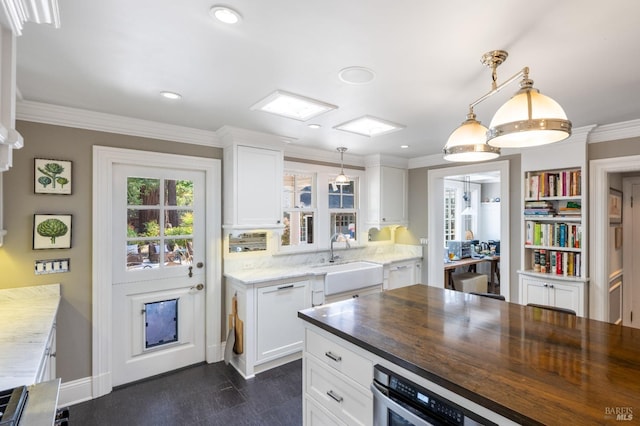 kitchen with white cabinets, wood counters, pendant lighting, and a sink
