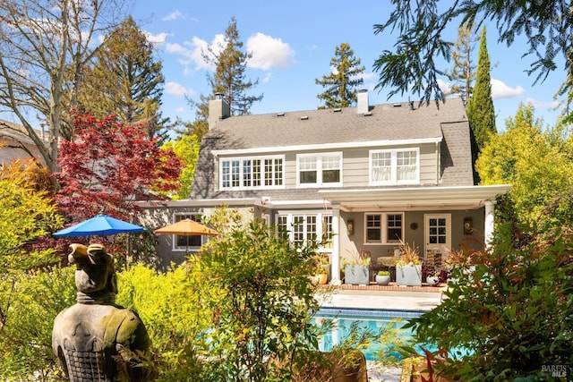 rear view of house featuring a patio, an outdoor pool, and a chimney