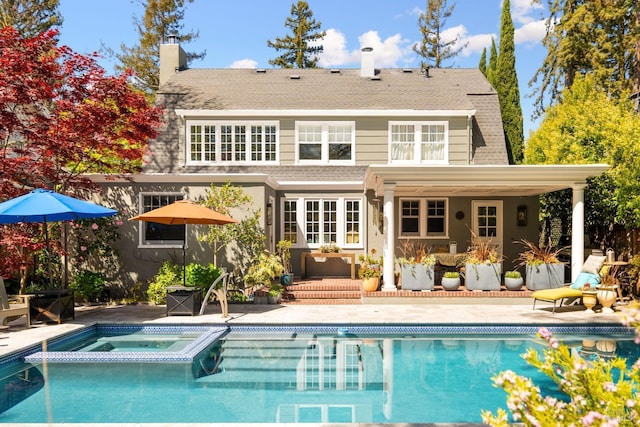 back of house featuring a shingled roof, a patio, a chimney, and a pool with connected hot tub