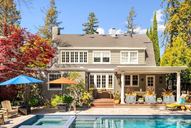 back of property with an in ground hot tub, a chimney, an outdoor pool, and a patio area