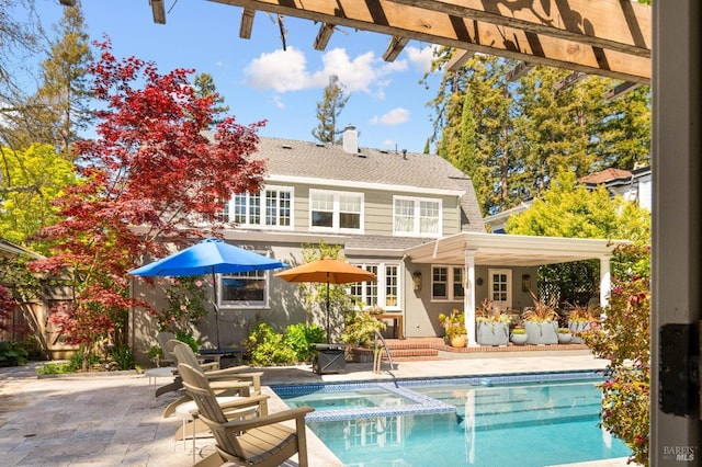 rear view of house featuring a patio, a shingled roof, a pool with connected hot tub, and a chimney