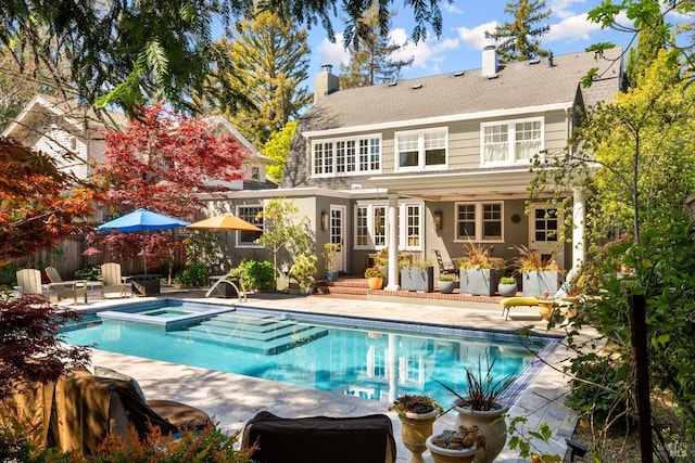 back of property with a patio area, a pool with connected hot tub, and a chimney