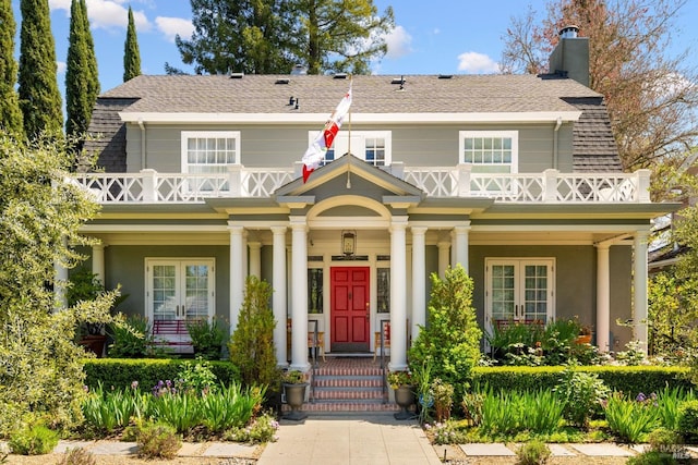 view of front of home with covered porch, stucco siding, french doors, a chimney, and a shingled roof