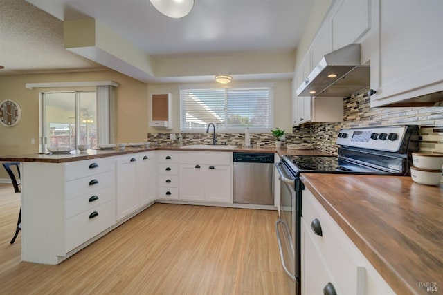 kitchen featuring a peninsula, wood counters, wall chimney exhaust hood, appliances with stainless steel finishes, and a sink