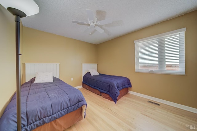 bedroom featuring a textured ceiling, visible vents, baseboards, wood finished floors, and a ceiling fan