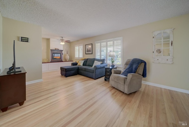 living area featuring baseboards, light wood-style flooring, a tile fireplace, and a textured ceiling