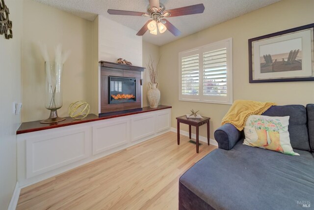 bedroom with baseboards, a textured ceiling, a glass covered fireplace, and light wood-style floors