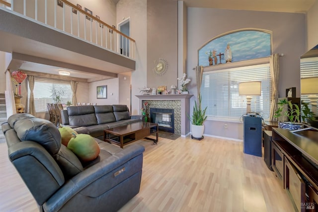 living area featuring stairway, a high ceiling, light wood-style floors, baseboards, and a tiled fireplace