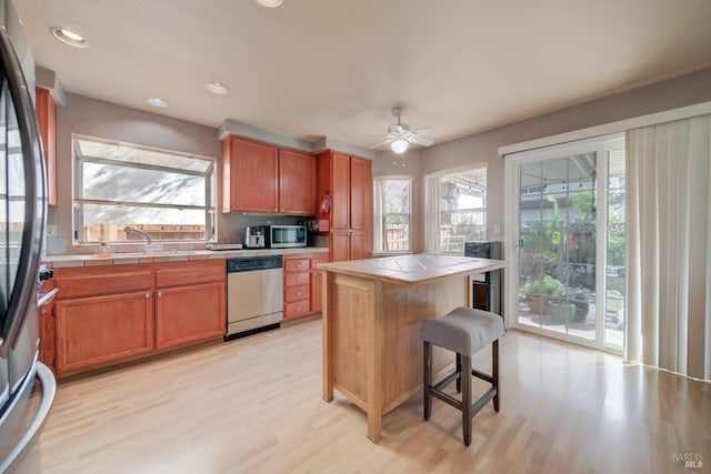 kitchen with tile countertops, a healthy amount of sunlight, stainless steel appliances, and light wood-style floors
