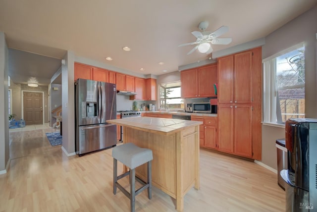 kitchen featuring a center island, tile counters, light wood-type flooring, appliances with stainless steel finishes, and under cabinet range hood