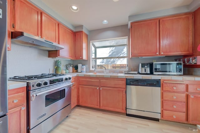kitchen with recessed lighting, under cabinet range hood, tile countertops, light wood-style floors, and appliances with stainless steel finishes
