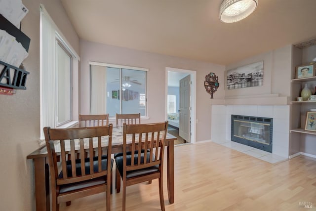 dining space with wood finished floors, a tiled fireplace, and baseboards
