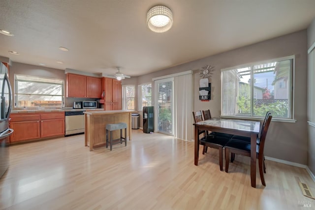 kitchen featuring a center island, brown cabinets, light wood-type flooring, stainless steel microwave, and dishwashing machine