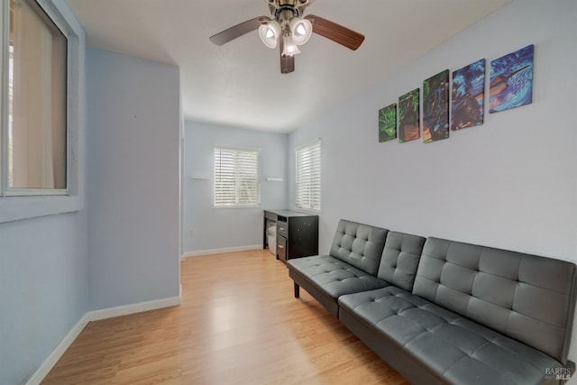 living room featuring baseboards, a ceiling fan, and light wood finished floors