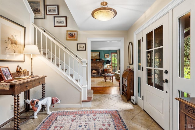 entryway featuring stairway, a warm lit fireplace, and light tile patterned flooring
