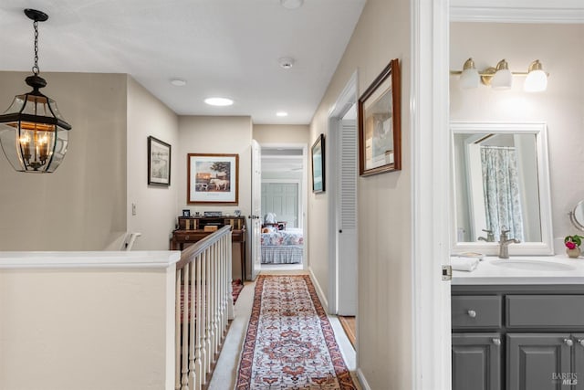hallway featuring recessed lighting, a chandelier, baseboards, and a sink