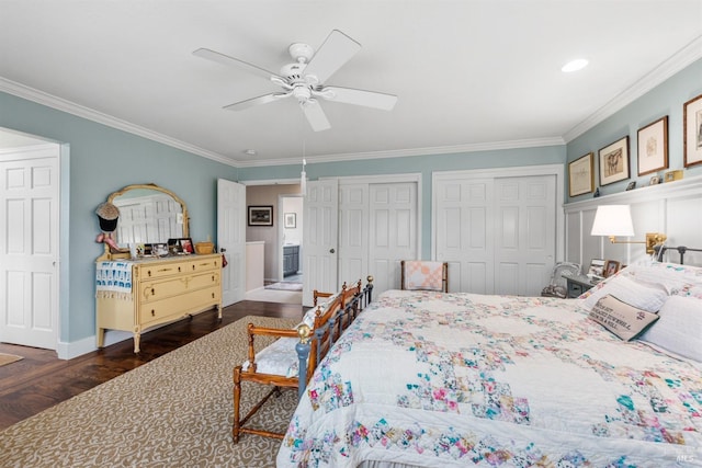 bedroom with crown molding, baseboards, wood finished floors, ceiling fan, and two closets