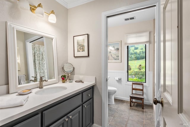 bathroom with crown molding, vanity, a wainscoted wall, toilet, and visible vents