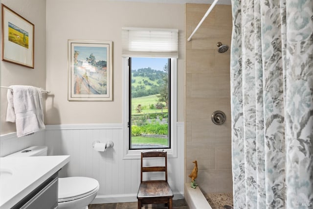 bathroom featuring toilet, a wainscoted wall, vanity, and a tile shower