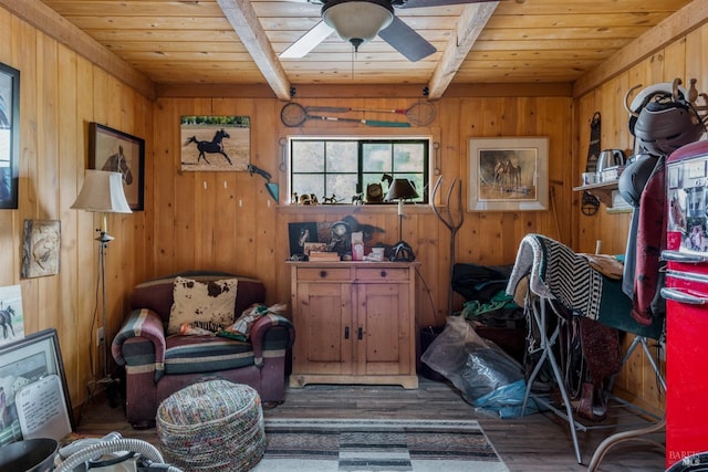 living area with beam ceiling, wood walls, wood ceiling, and a ceiling fan