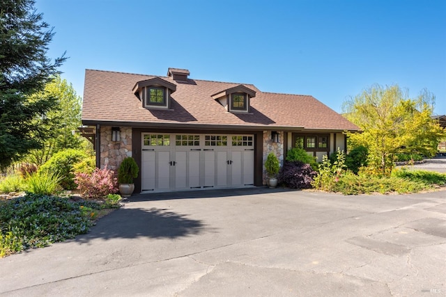 view of front of home with an attached garage, driveway, stone siding, and roof with shingles