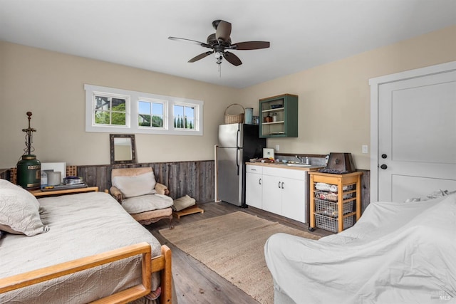 bedroom featuring freestanding refrigerator, wood finished floors, ceiling fan, and a sink