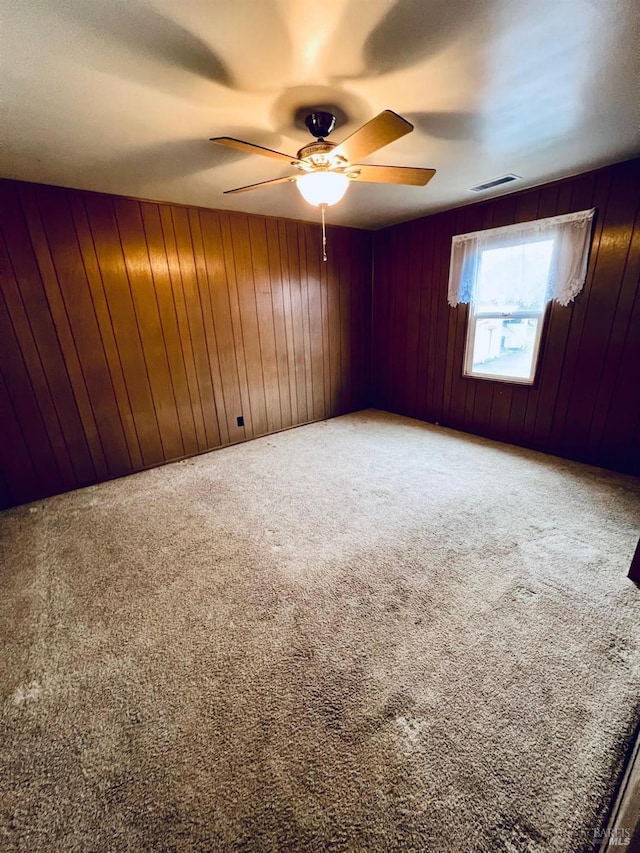 unfurnished room with carpet floors, wood walls, ceiling fan, and visible vents