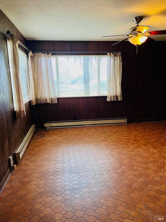 empty room with plenty of natural light, baseboard heating, and wood walls