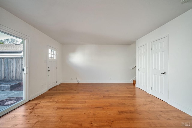 unfurnished room featuring baseboards, stairs, and light wood-style floors