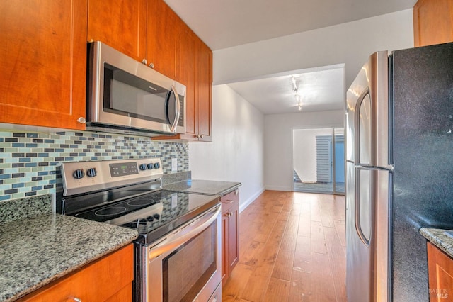 kitchen with light wood finished floors, light stone countertops, tasteful backsplash, appliances with stainless steel finishes, and brown cabinetry