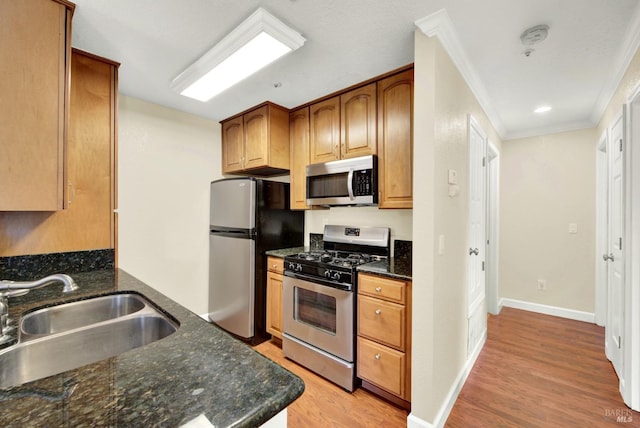 kitchen featuring stainless steel appliances, light wood-style flooring, a sink, dark stone countertops, and crown molding